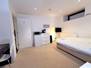 A hotel room with a bed, a desk, a chair, a dresser, a microwave, a TV, and a lamp. - Spacious Double Room with en-suite - 2b (London)