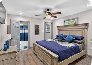 A bedroom with a bed, a ceiling fan, a window, and a door.