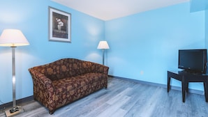 Una habitación con un sofá, dos lámparas de pie, un televisor sobre un mueble bajo y un cuadro en la pared.