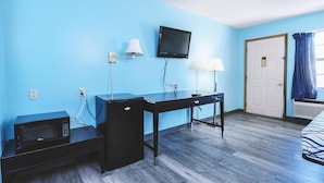 Una habitación pequeña con escritorio, dos lámparas, televisor, microondas y una puerta.