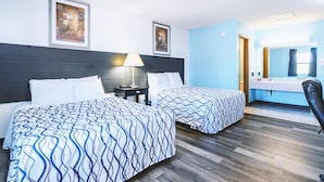 Habitación de hotel con dos camas, una mesita de noche, una lámpara, un espejo y un baño con lavabo y espejo.