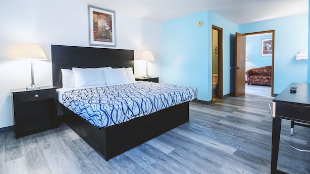 Un dormitorio con una cama, dos mesitas de noche con lámparas, una puerta que da a otra habitación y una pequeña mesa con un control remoto.