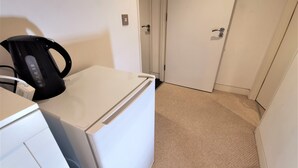 A compact kitchen with a white refrigerator, a black kettle, and a white countertop. - Spacious Double Room with en-suite - 2c (London)