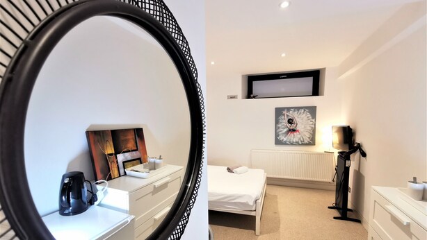 A hotel room with a bed, a TV mounted on the wall, a painting, a radiator, and a mirror with a black frame. - Spacious Double Room with en-suite - 2c (London)