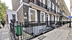 A row of terraced houses with black metal fences, a green trash bin, and a blue directional sign on the sidewalk. - Spacious Double Room with en-suite - 2c (London)