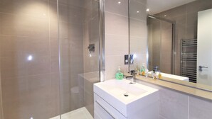 A modern bathroom with a glass-enclosed shower, a white vanity with a large mirror, and a towel rack. - Spacious Double Room with en-suite - 2c (London)