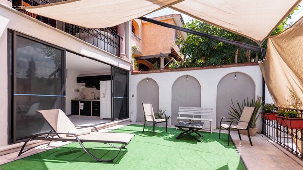 An outdoor patio with a green artificial turf, a white bench, and two lounge chairs.