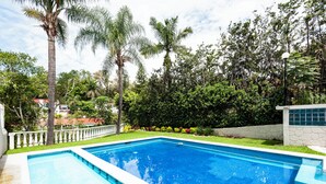 A rectangular swimming pool with clear blue water, surrounded by a well-maintained lawn and various trees.