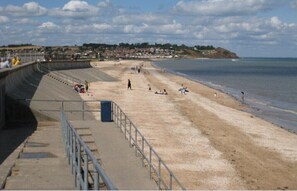 Une plage bordée d’une barrière en béton, avec des marches descendant vers le rivage, et une ville visible au loin.