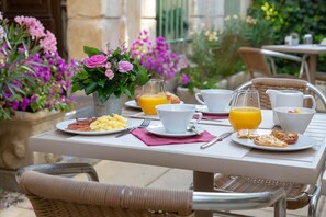 A breakfast table set outdoors with plates of food, a pitcher of orange juice, and a vase of flowers. - Hotel Le Relais De Poste (Arles)