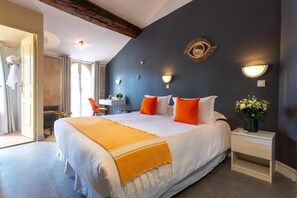 Quarto de hotel com uma cama grande, uma pequena mesa de escritório, uma cadeira e mesa de cabeceira com um vaso de flores.