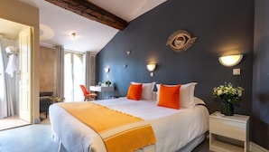 A hotel room with a large bed, a small desk, a chair, and a nightstand with a vase of flowers. - Hotel Le Relais De Poste (Arles)