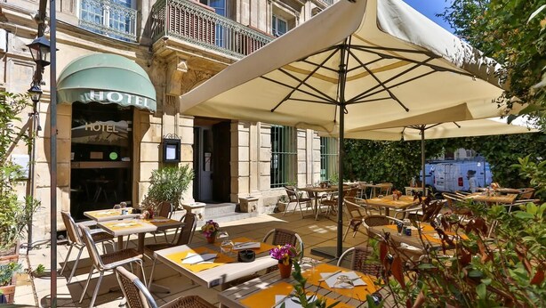 An outdoor hotel patio with tables and chairs, a large umbrella, and a building entrance labeled 'HOTEL'. - Hotel Le Relais De Poste (Arles)