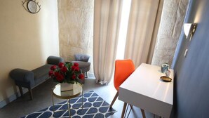 A room with a sofa, a chair, a small table with a vase of flowers, and a window with curtains. - Hotel Le Relais De Poste (Arles)