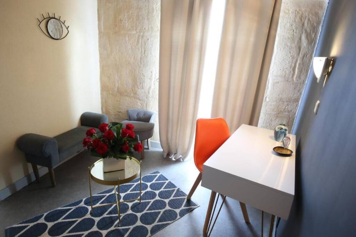 Ein Zimmer mit einer Couch, einem Sessel, einem kleinen Tisch mit Blumenvase und einem Fenster mit Vorhängen.