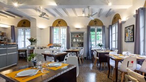 Un comedor con mesas dispuestas para comidas, una cocina al fondo y un techo con vigas a la vista.