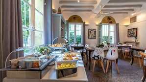 A dining area with buffet-style food, tables, chairs, and large windows. - Hotel Le Relais De Poste (Arles)