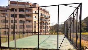 A tennis court enclosed by a chain-link fence with a multi-story building in the background. - Holiday Park (Varna)