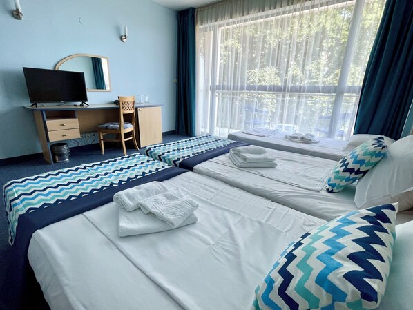 Une chambre d’hôtel avec deux lits, un bureau, une chaise, une télévision et une fenêtre avec des rideaux.