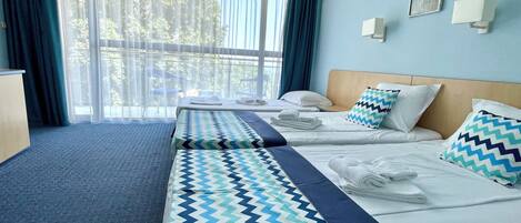 A hotel room with two beds, a desk, and a large window with curtains.