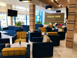 A modern lounge area with sofas and armchairs, a reception desk, and a large window offering a view of greenery.