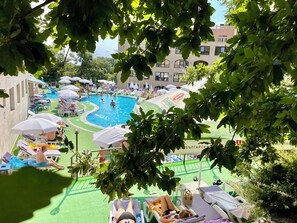 A swimming pool area with lounge chairs and umbrellas, surrounded by greenery and buildings. - Holiday Park (Varna)