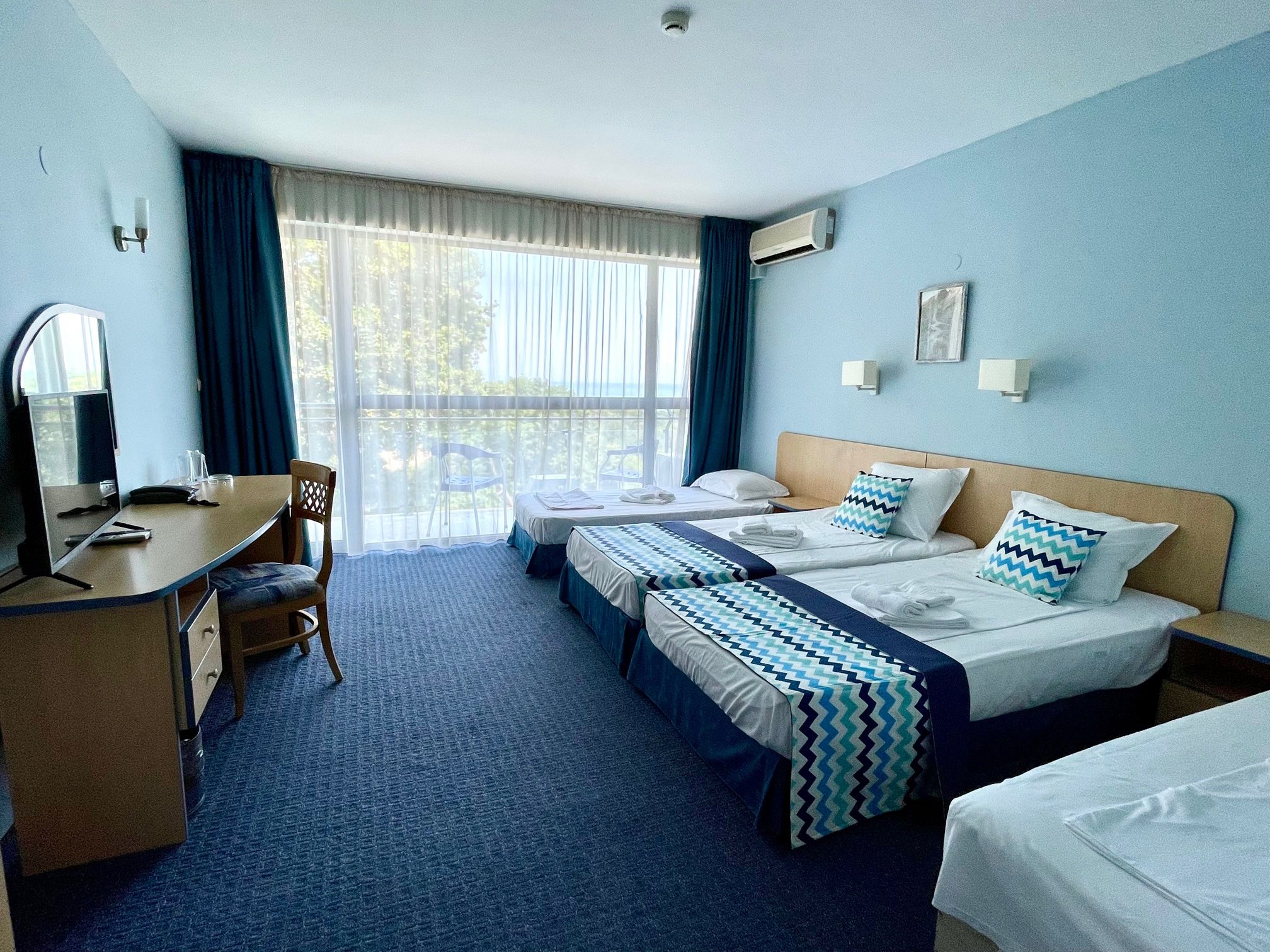 A hotel room with two beds, a desk, a chair, and a window with curtains.