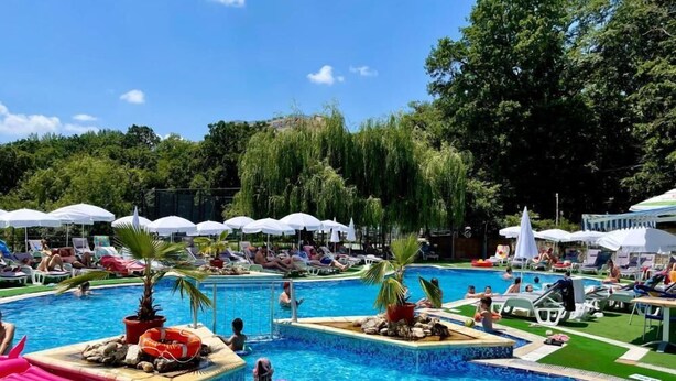 A pool area with multiple sections, lounge chairs, umbrellas, and a small waterfall feature. - Holiday Park (Varna)