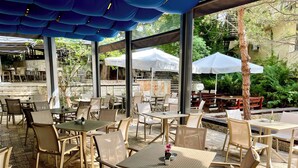 An outdoor seating area with tables and chairs, covered by a blue canopy, and surrounded by greenery. - Holiday Park (Varna)