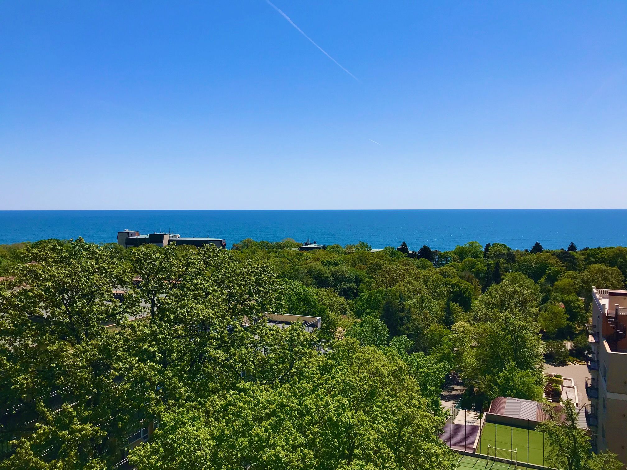 A residential area with a view of the sea, surrounded by greenery and buildings.