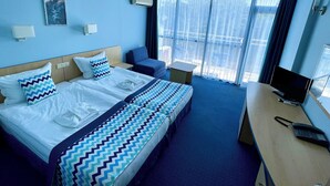 A hotel room with a bed, a desk, a chair, a TV, and a window with curtains. - Holiday Park (Varna)