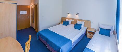 A hotel room with a bed, bedside tables, a chair, a desk, and an air conditioning unit.