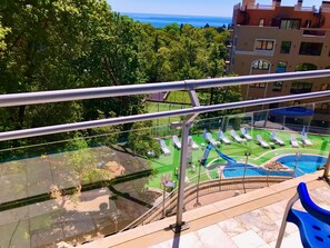 A pool area with lounge chairs and a slide, surrounded by trees and buildings. - Holiday Park (Varna)