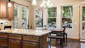Una cucina con piani in granito, mobili in legno e un'isola grande. Diverse finestre offrono vista su una zona rocciosa all'esterno.