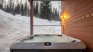 Vasca idromassaggio in un ambiente innevato con parete di una baita in legno e un pontile in legno.