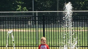 Un niño de pie cerca de una fuente de agua en un parque.