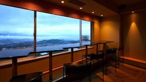 A room with large windows offering a view of a city and mountains. There are tables and chairs arranged for dining or sitting. - Yorokobi no Yado Shinki (Shibukawa)
