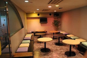 A room with multiple round tables and cushioned seating areas, a flat-screen TV mounted on the wall, and a potted plant.