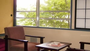 A room with a single chair and a small table, a window with a view of trees, and a radiator on the wall. - Yorokobi no Yado Shinki (Shibukawa)