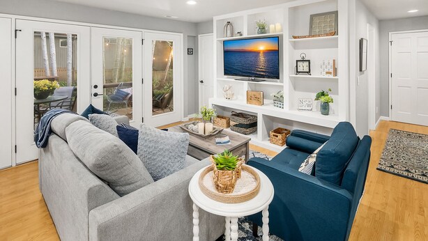 A living room with a grey sofa, a blue sofa, a TV on the wall, and a small table with a plant.