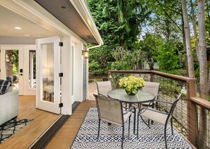 A patio area with a round table, chairs, and a potted plant. There is a wooden deck and a patterned rug.