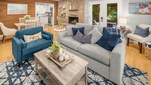 A living room with a blue sofa, a grey sofa, and a wooden coffee table. There is a fireplace, a dining table, and a kitchen in the background.