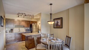 A kitchen with wooden cabinets, a central island, a dining table with chairs, a chandelier, and a framed picture on the wall. - Ski In-Out on 4Oclock with Chair and Town Access! (Breckenridge)