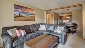 A living room with a grey sectional sofa, a wooden coffee table, and a painting of a landscape. - Ski In-Out on 4Oclock with Chair and Town Access! (Breckenridge)