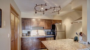 A kitchen with wooden cabinets, a granite countertop, a stainless steel refrigerator, a microwave, and a coffee maker. - Ski In-Out on 4Oclock with Chair and Town Access! (Breckenridge)