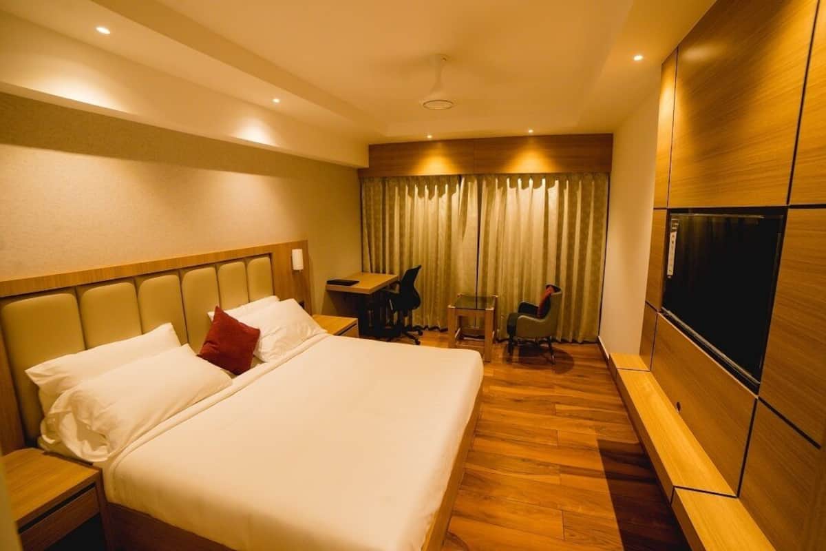 A hotel room with a large bed, a desk, a chair, a TV, and a curtain.