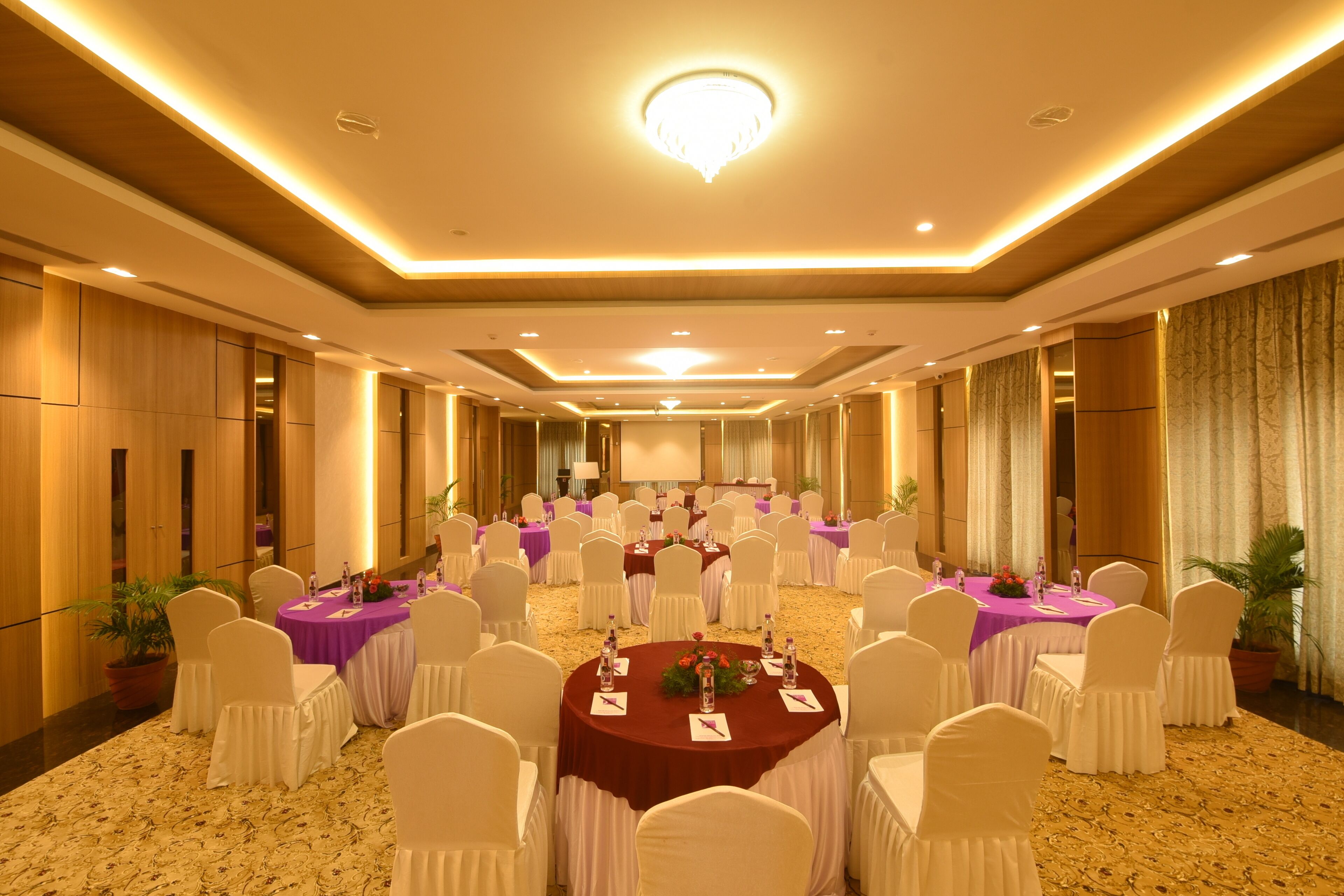 A conference room with round tables, white chairs, and a stage.