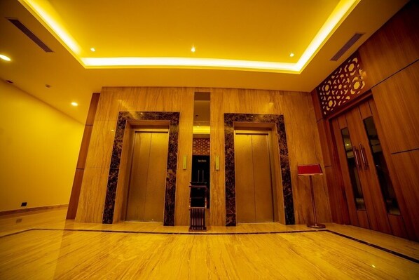 A spacious lobby with a marble floor, wooden paneling, and a modern ceiling design.