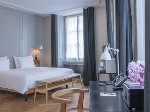 A hotel room with a bed, bedside table, lamp, desk with phone and calculator, and a view of the outdoors through the window. - Marktgasse Hotel (Zürich)