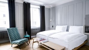 Une chambre d’hôtel avec un grand lit, une chaise, une petite table et une vue sur la ville par la fenêtre.
